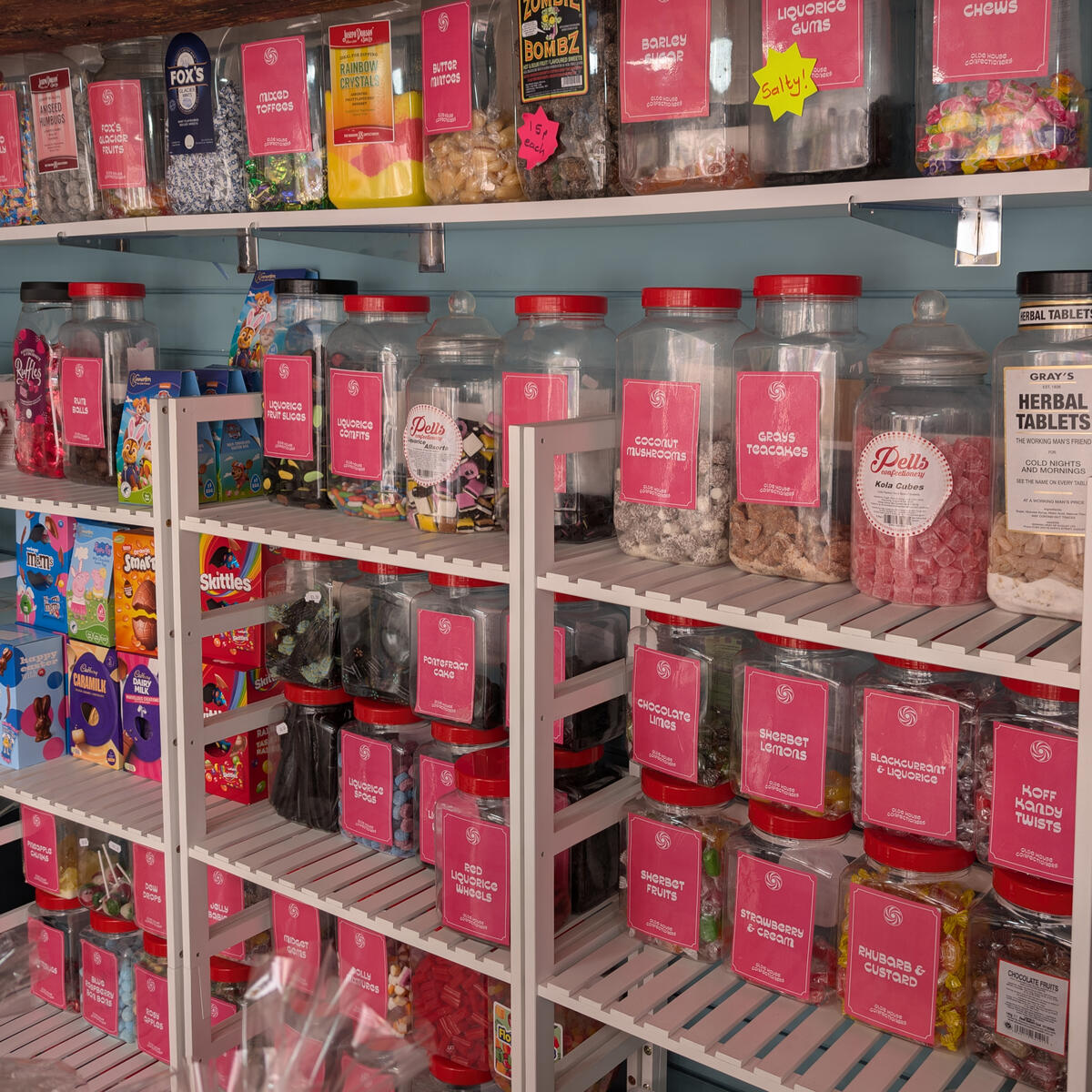 A selection of traditional sweets in pink tubs on white shelves.
